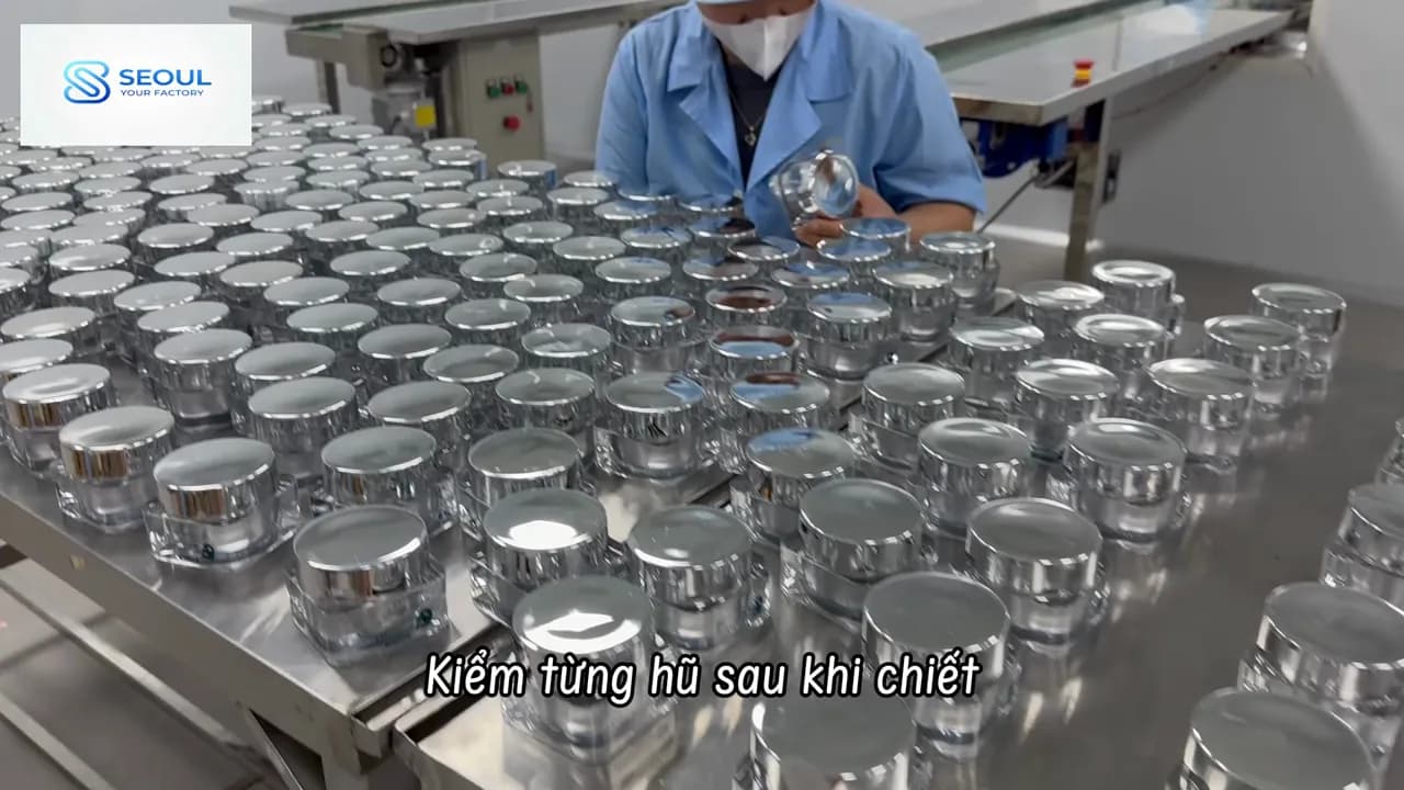 Công nhân kiểm từng hũ kem nắp bạc trên bàn inox sau khi chiết