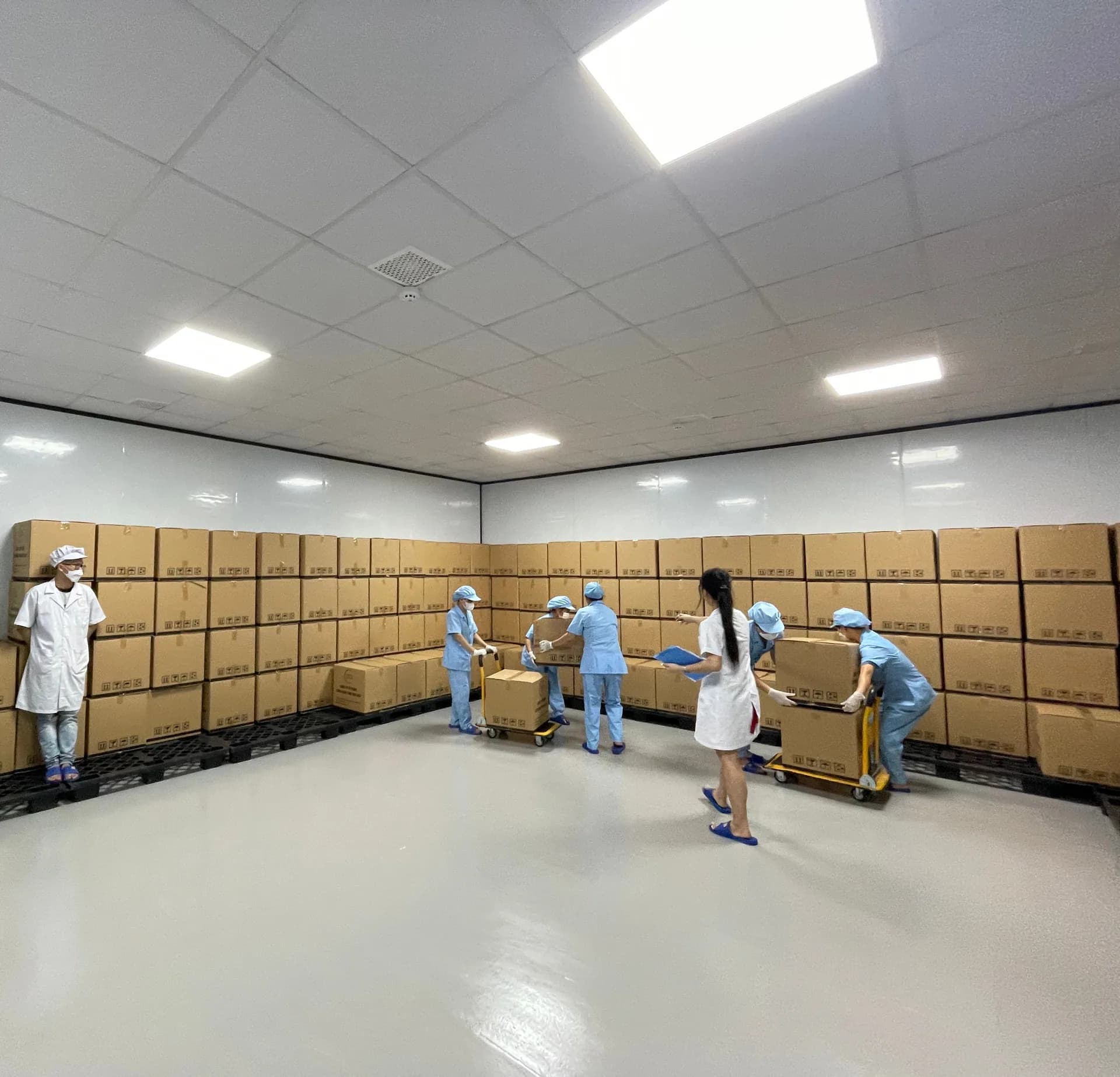 Kho thành phẩm với các thùng hàng xếp trên pallet và công nhân vận chuyển