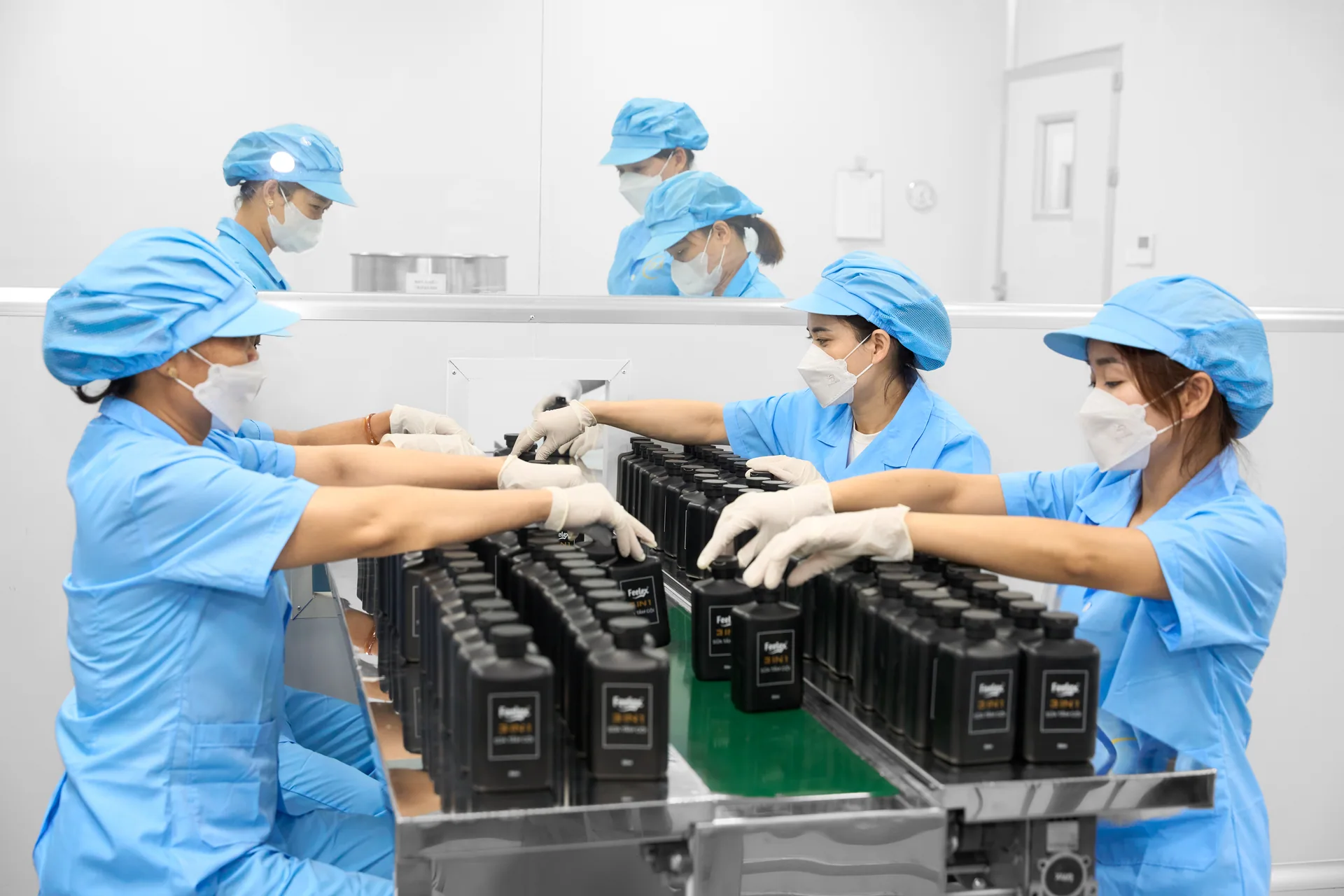 Công nhân đóng gói chai dầu gội thành phẩm trên băng chuyền