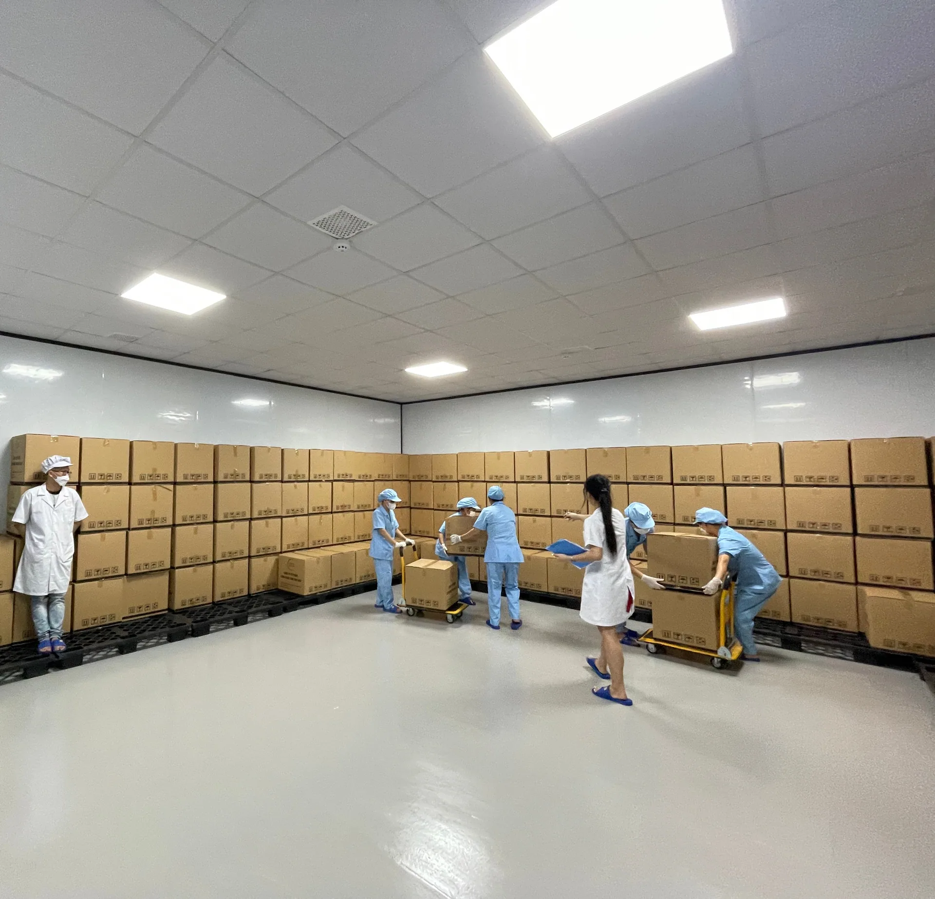 Kho thành phẩm với các thùng hàng xếp trên pallet và công nhân vận chuyển